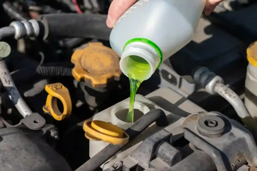 Hand with bottle pouring antifreeze coolant into the expansion tank