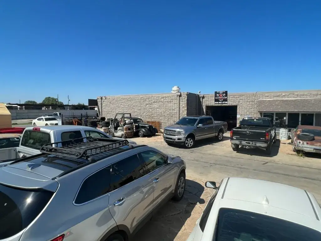 Outside view of T Autocare Takedown auto repair shop in Broken Arrow, showing multiple parked vehicles and a clear blue sky.