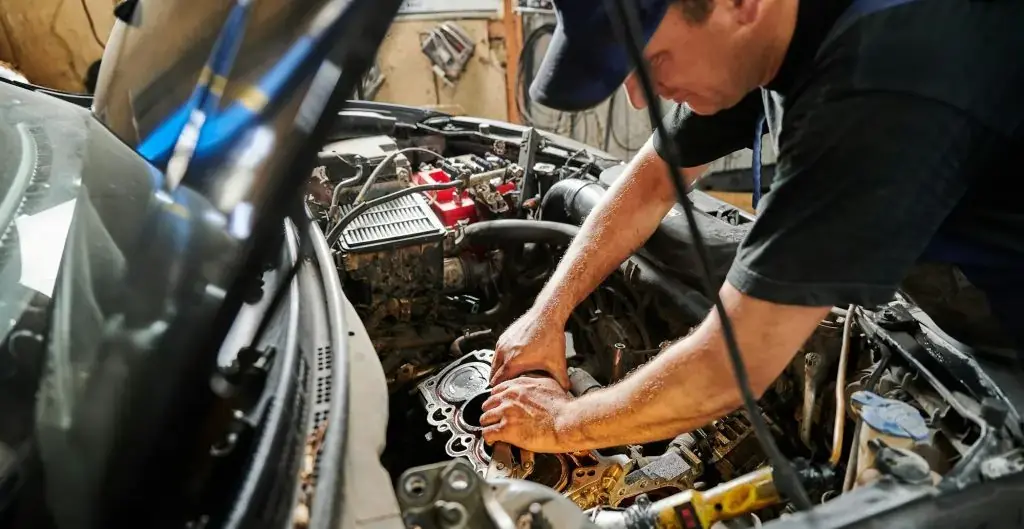 Worker, repairman wearing cap, repairing car engine.